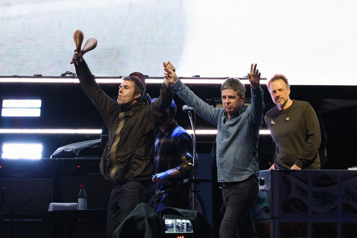 Liam Gallagher e Noel Gallagher sul palco che salutano a mani alzate i fan