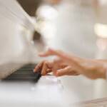 Primo piano di mani che suonano un pianoforte bianco.